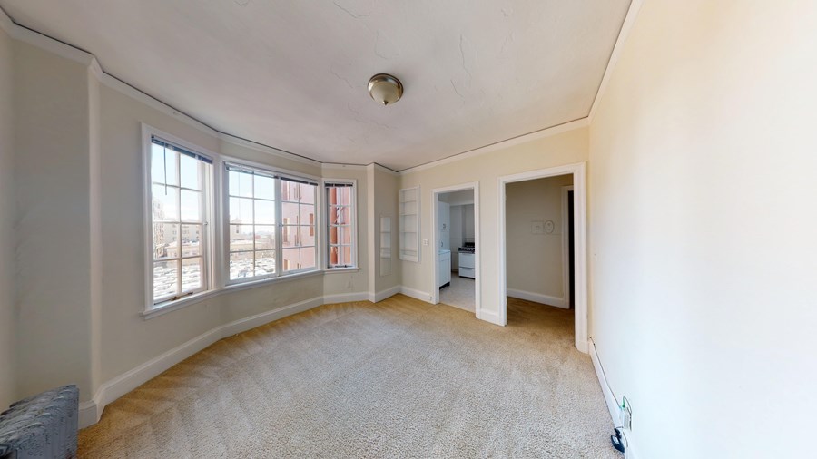 A room with a carpeted floor and a window with a view of a building outside.
